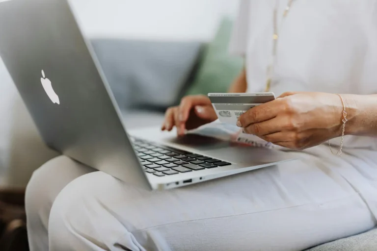 Pessoa fazendo compra online com cartão de crédito utilizando um laptop da Apple, simbolizando compras digitais e segurança financeira.